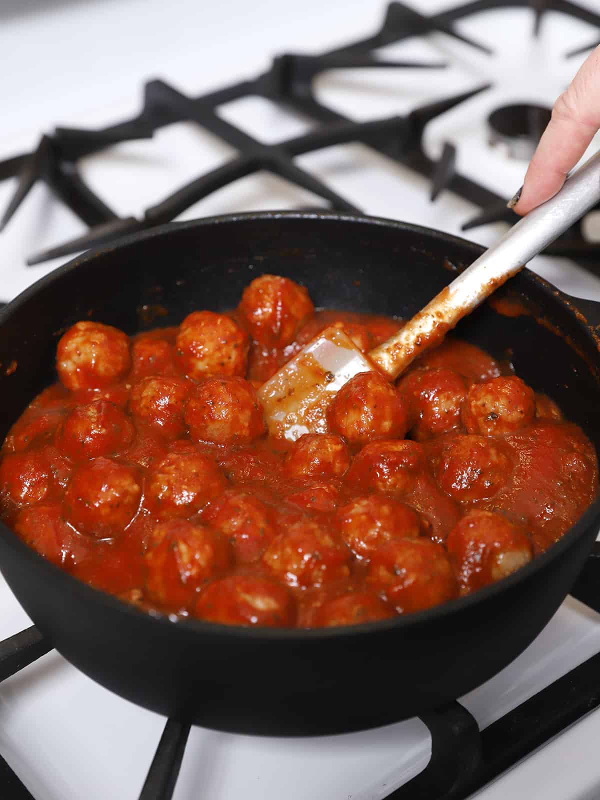 Frozen meatballs being stirred into the sauce. 