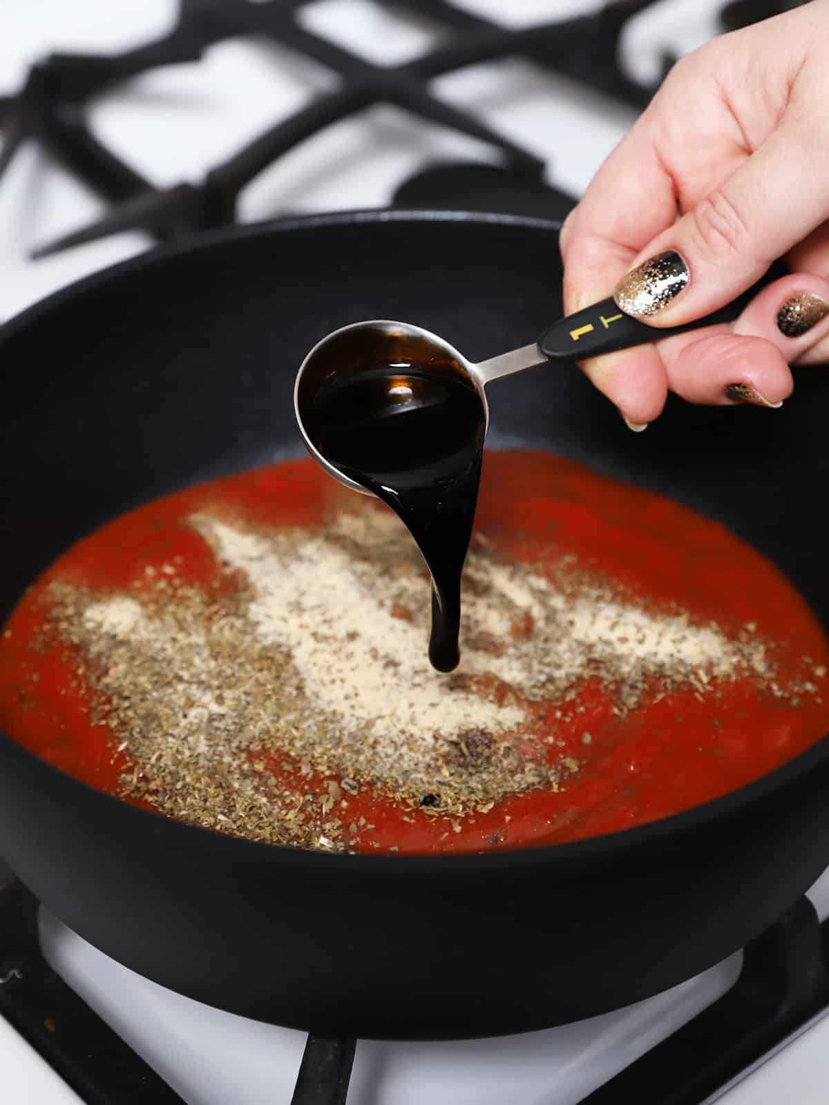 Balsamic vinegar being poured into a pan of sauce and herbs. 