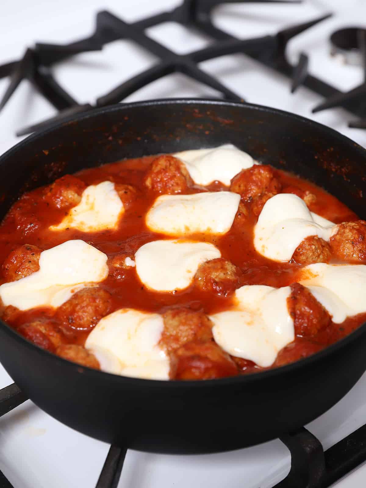 Mozzarella cheese sliced melted over a pan of meatballs. 