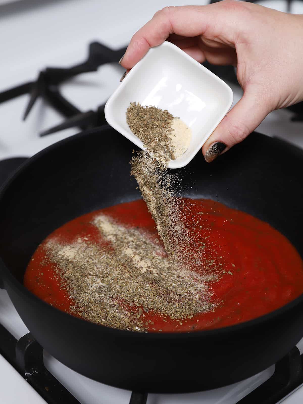 Spices being sprinkled into a pan of tomato sauce.