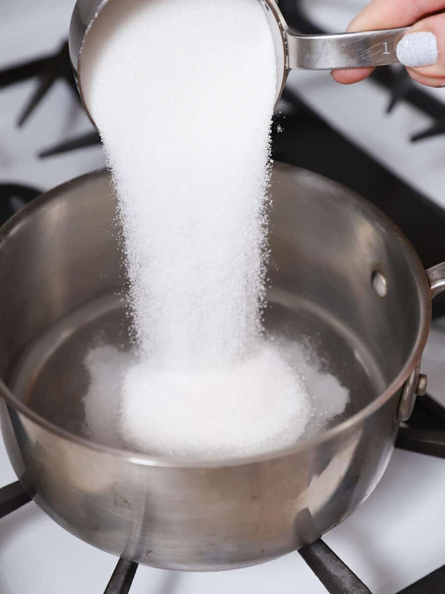 A hand pouring white sugar into a pot.