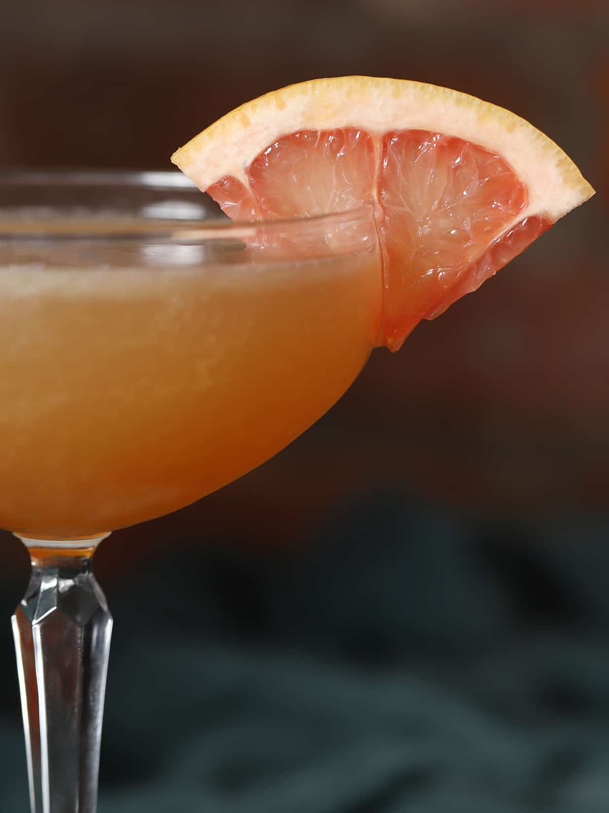 A slice of grapefruit garnishing a glass of brown derby cocktail. 