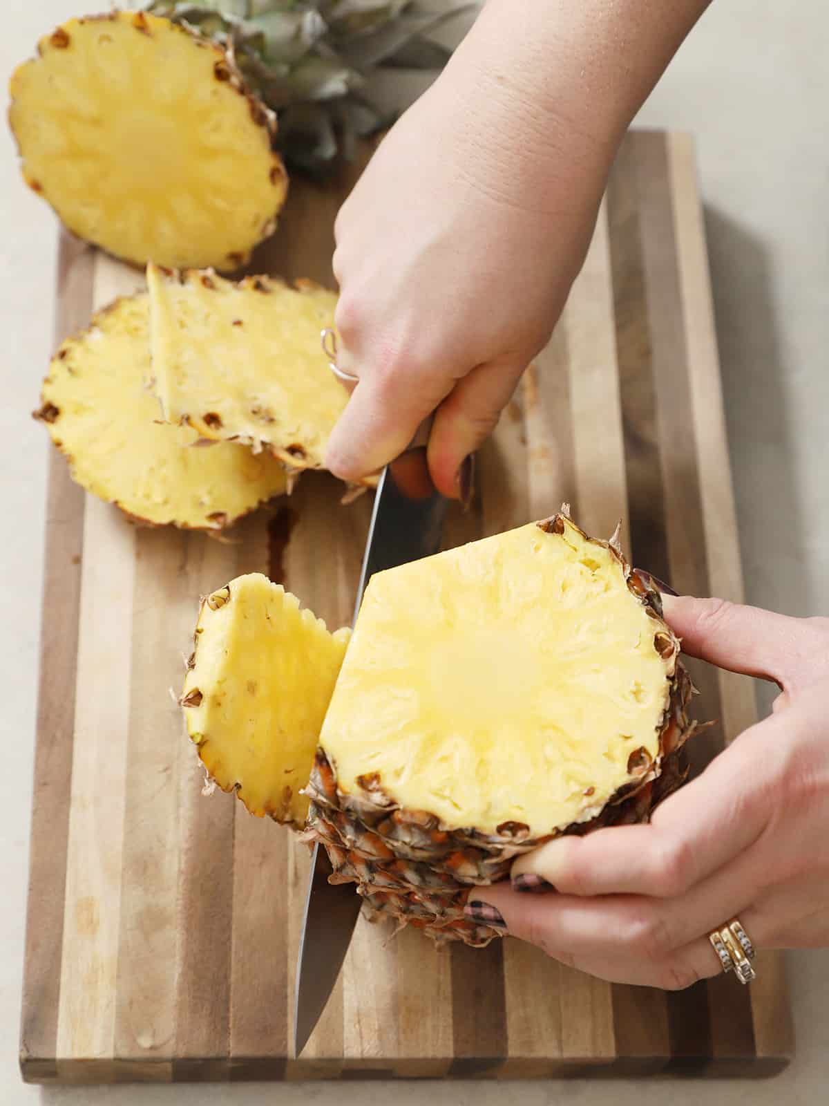 A hand cutting up a fresh pineapple. 
