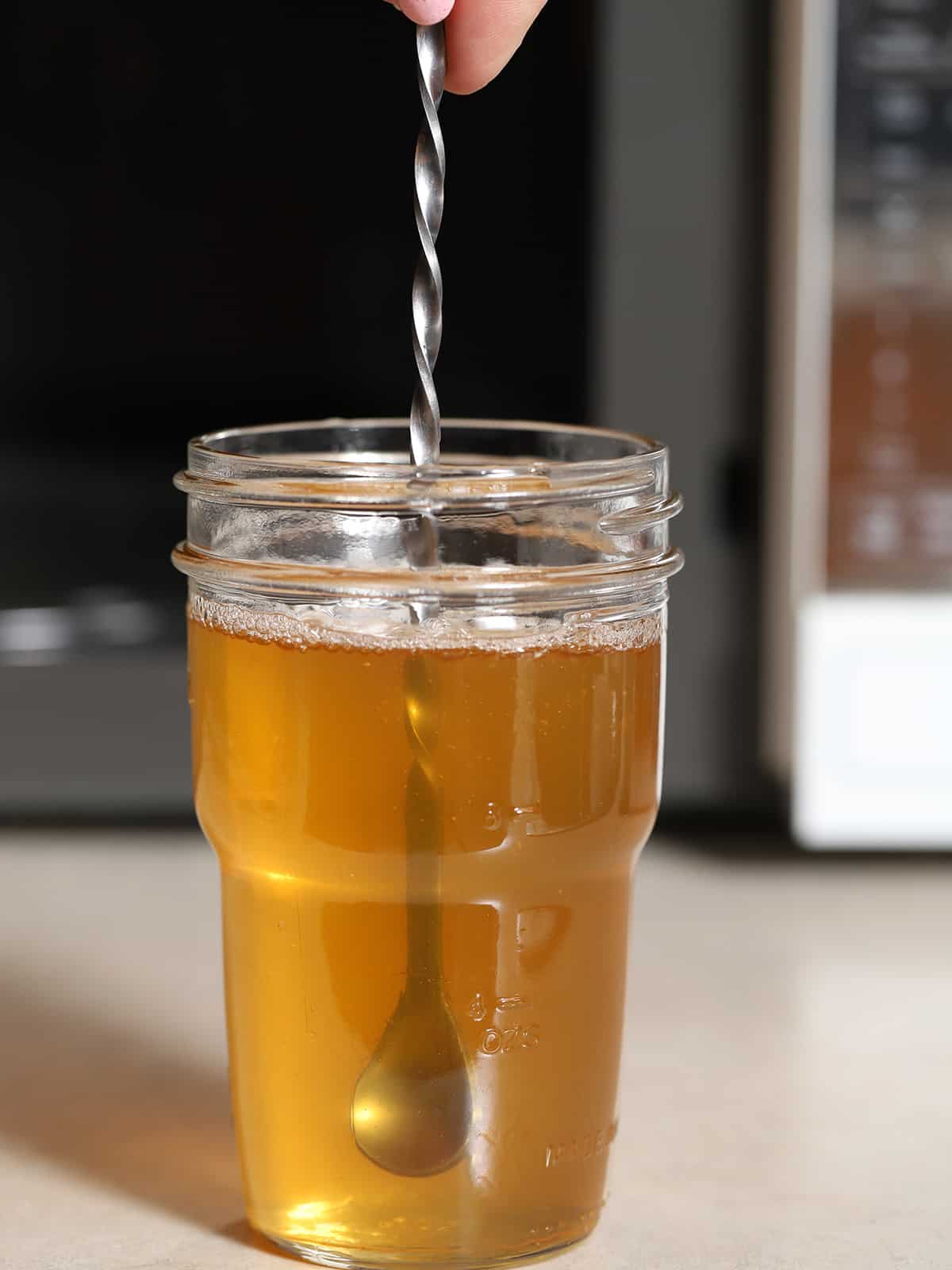 A hand stirring a jar of honey syrup. 