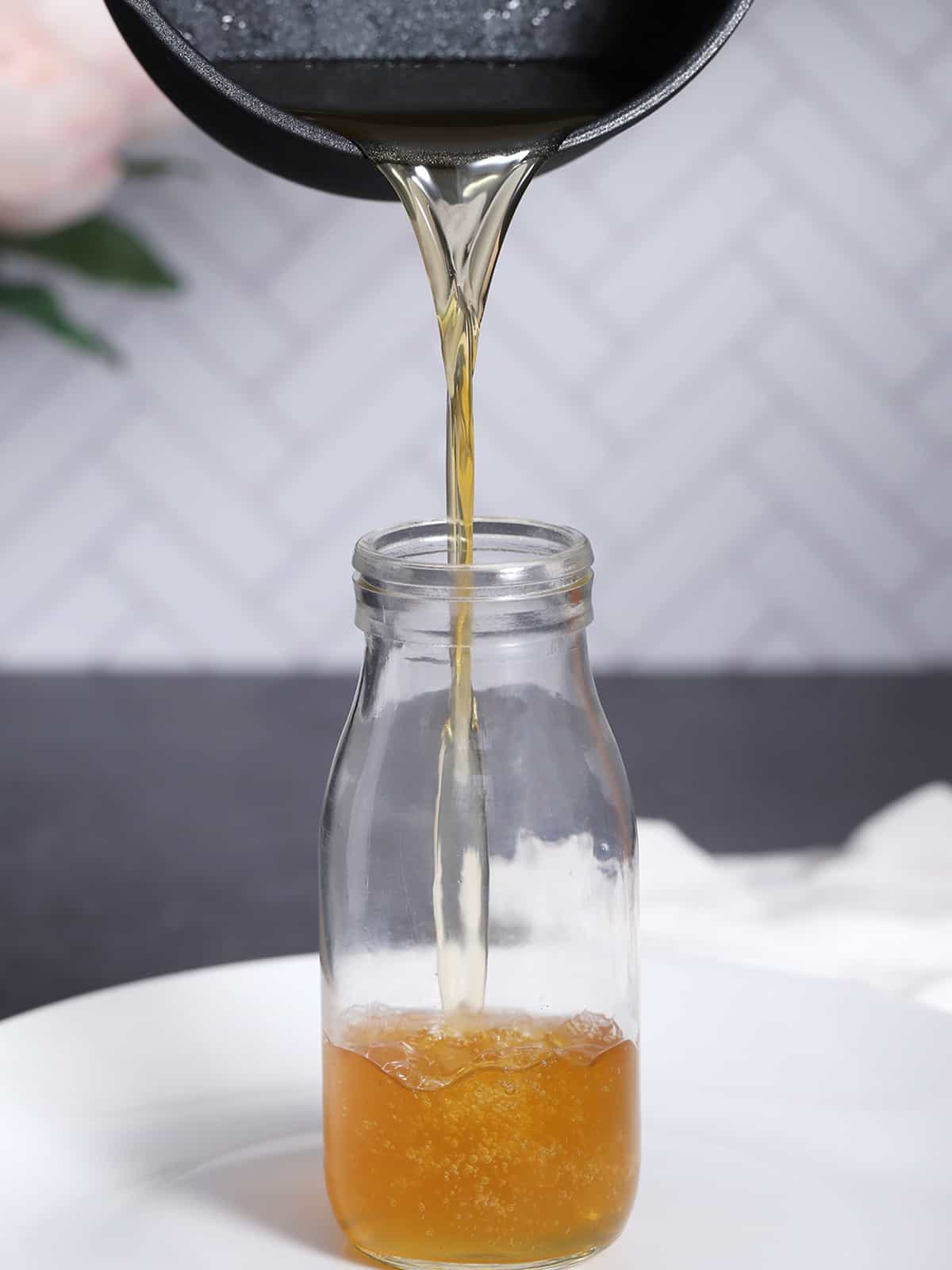 Honey syrup being poured from a pot into a bottle. 