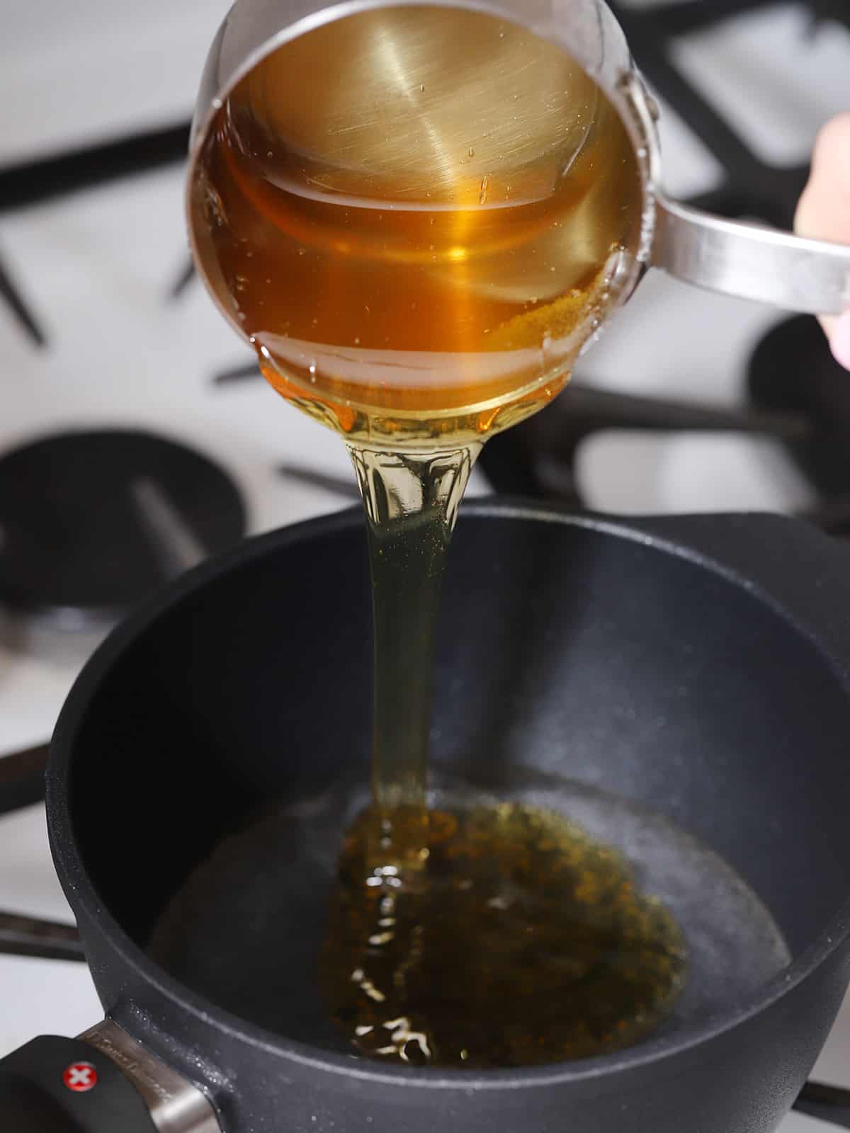Honey being poured into a pot on the stove. 