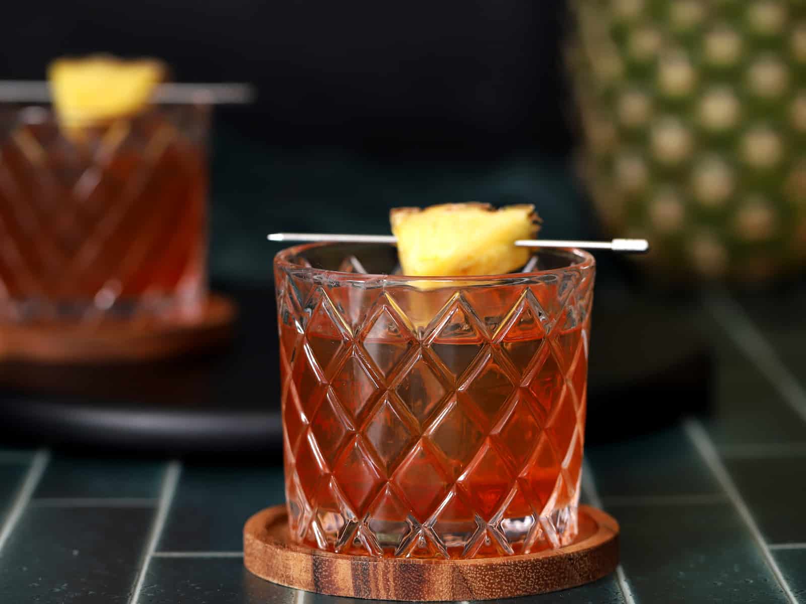A glass of pineapple old fashioned garnished with a pineapple wedge.