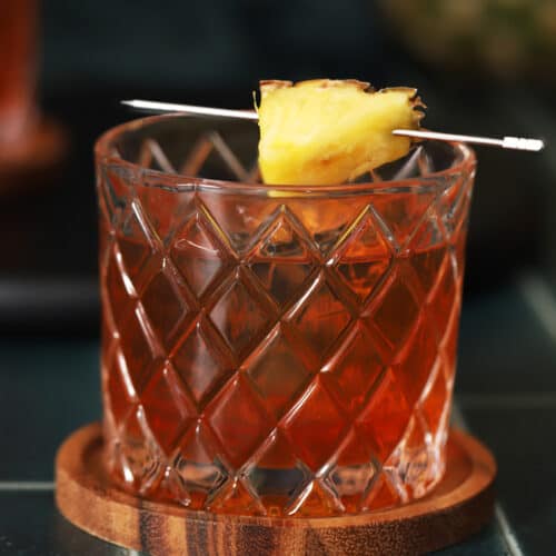 A glass of pineapple old fashioned garnished with a pineapple wedge.