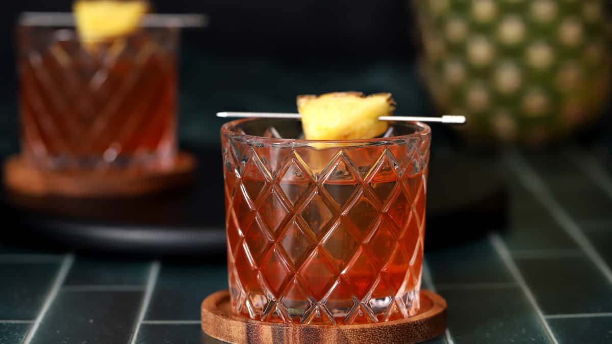 A glass of pineapple old fashioned garnished with a pineapple wedge. 