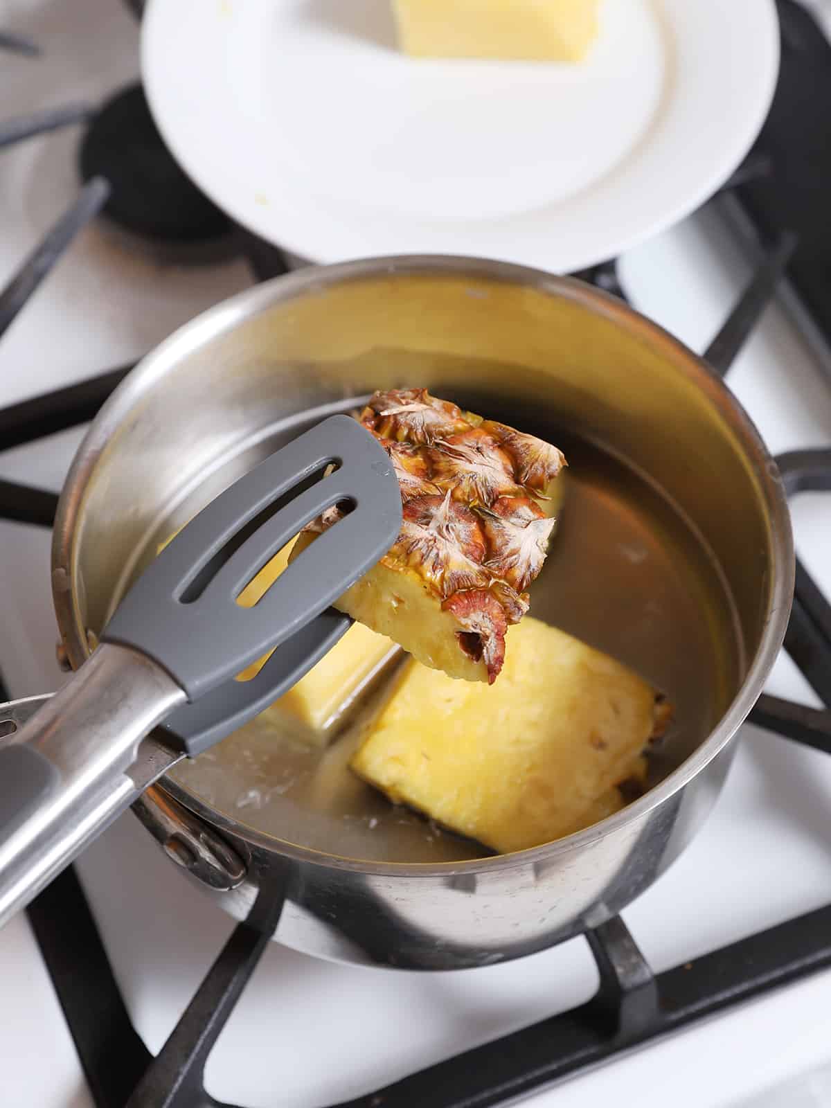 Tongs adding pieces of pineapple rind to a pot. 