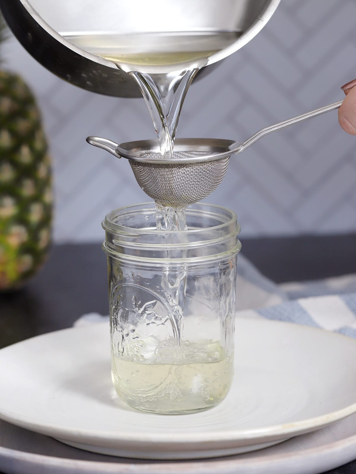 Pineapple syrup being poured through a fine mesh strainer into a mason jar. 