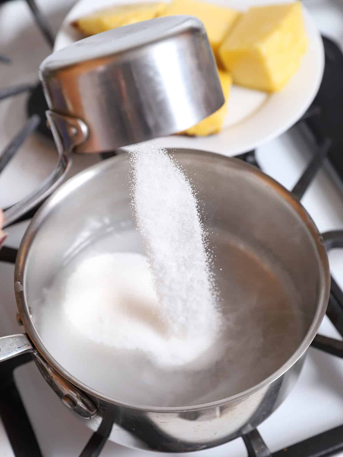 Sugar being poured into a pot of hot water. 