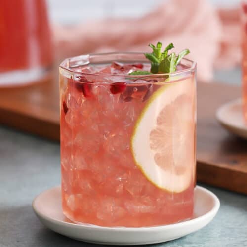 A glass of pomegranate lemonade garnished with a slice of lemon.