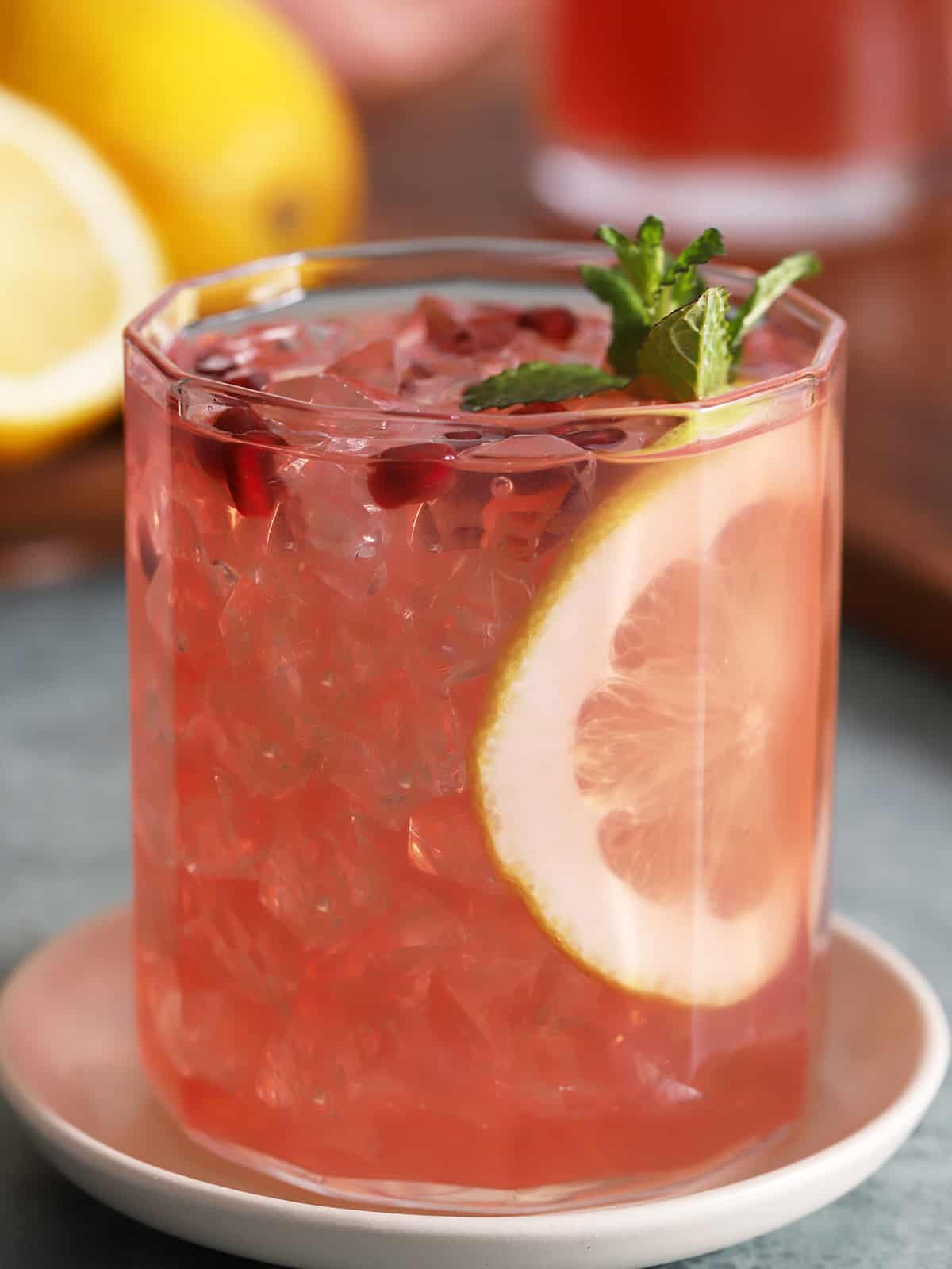 A glass of pomegranate lemonade garnished with a slice of lemon.