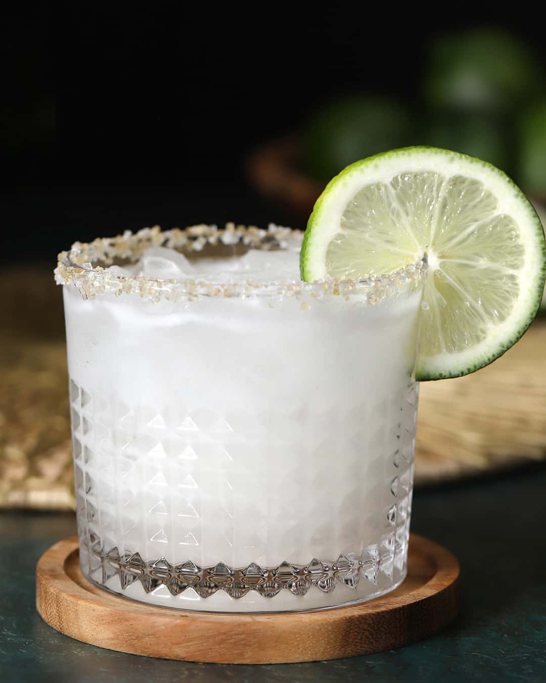 A glass of coconut margarita with a salt-sugar rim, garnished with a lime wheel.