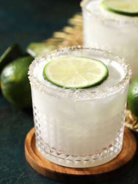 Glasses of coconut margarita with sugar rims and lime slices sitting on top of them.