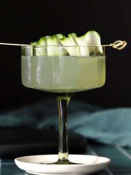 A coupe glass of cucumber martini garnished with a ribbon of cucumber peel.