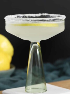 A coupe glass filled with lemon drop martini cocktail in front of a bowl of lemons.