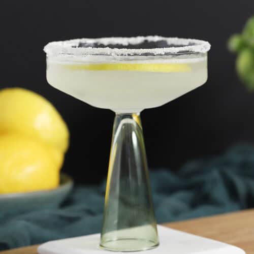 A coupe glass filled with lemon drop martini cocktail in front of a bowl of lemons.