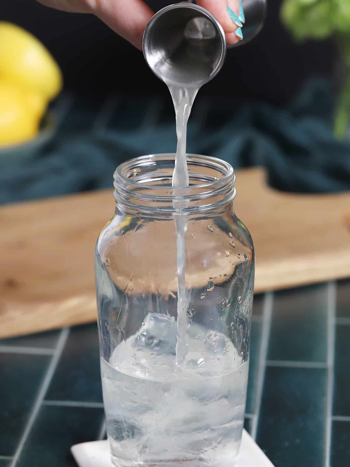 Lemon juice being poured into a glass cocktail shaker filled with ice cubes. 