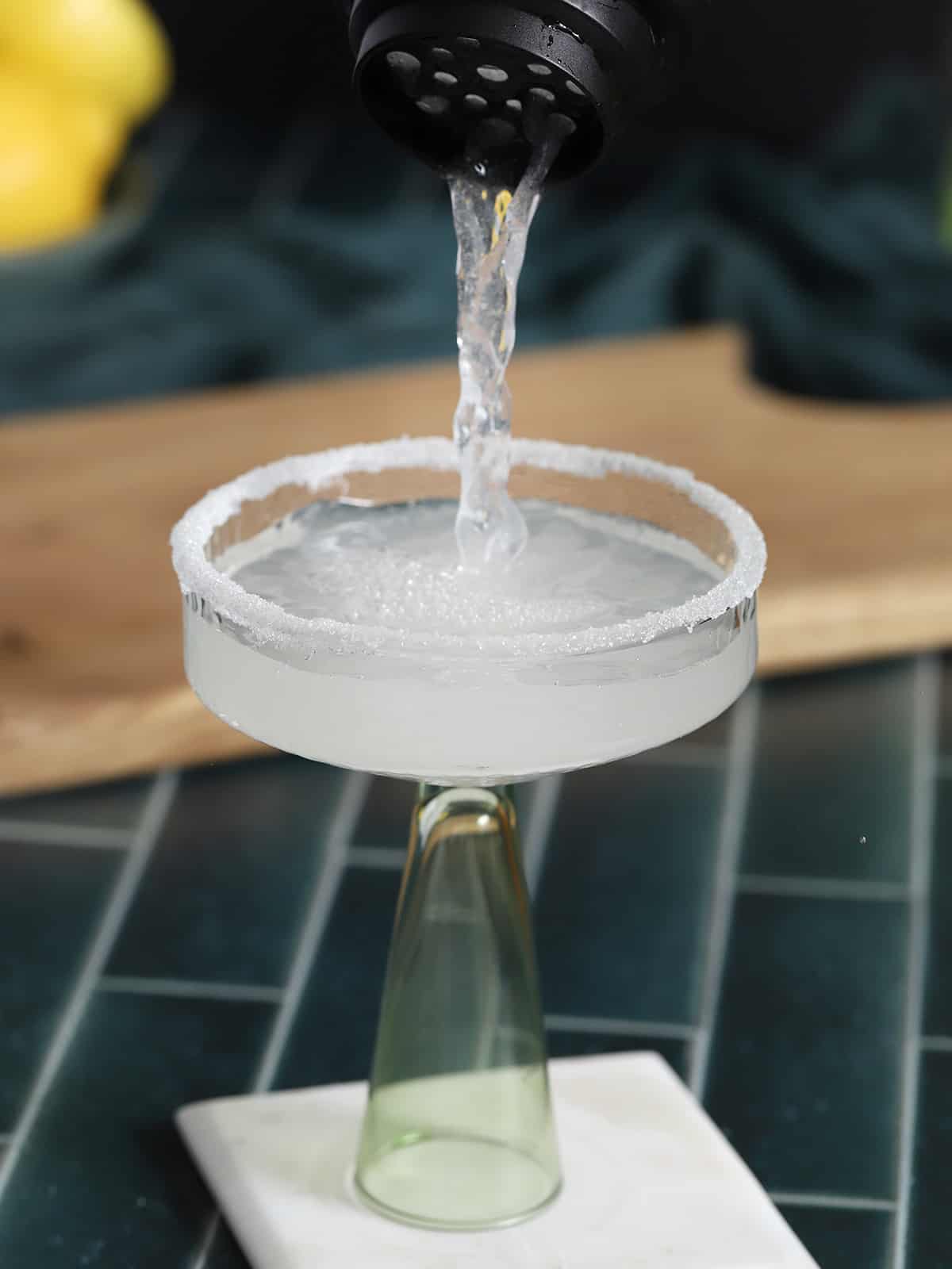 Lemon drop martini cocktail being poured from a cocktail shaker into a coupe glass. 