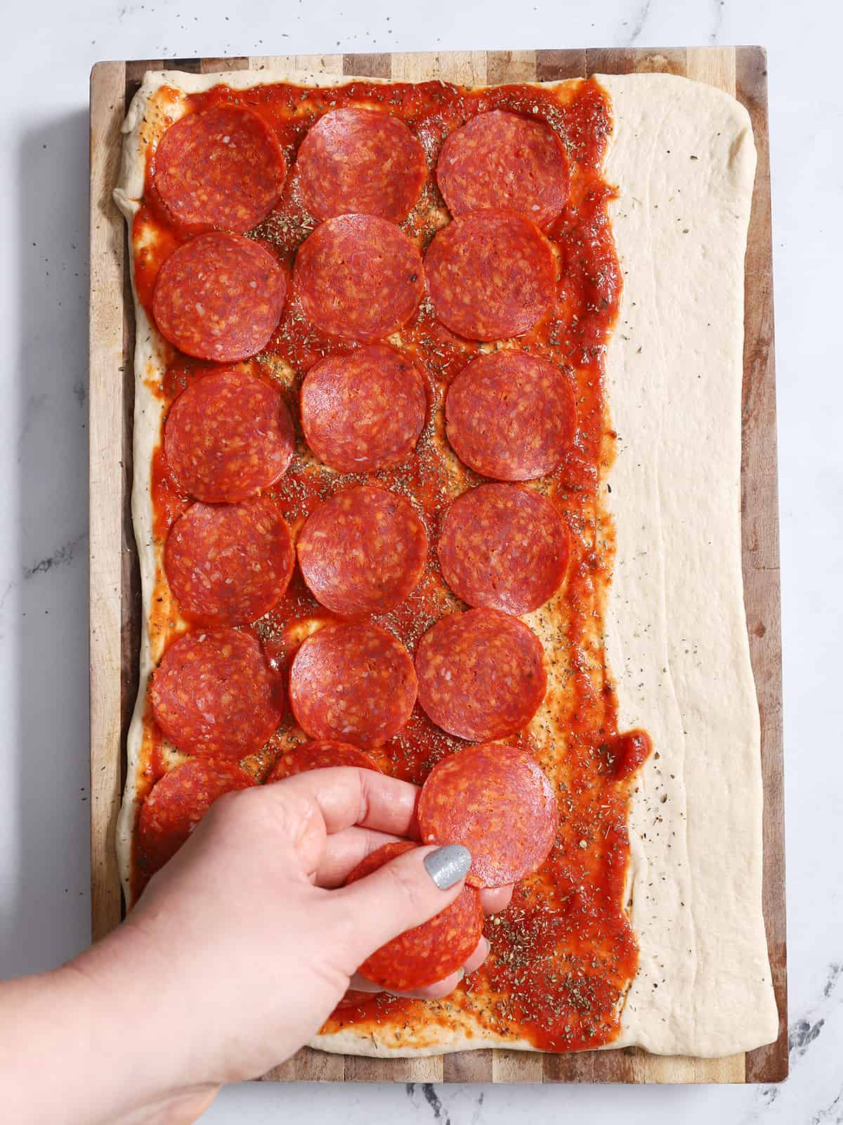 A hand placing pepperoni on pizza dough.