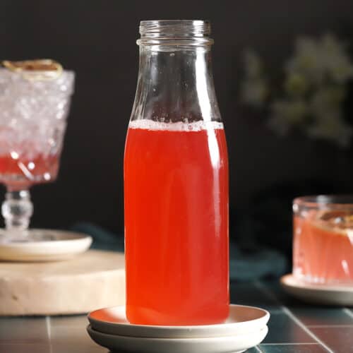 A bottle of rhubarb syrup in the middle of 2 glasses of rhubarb drinks.