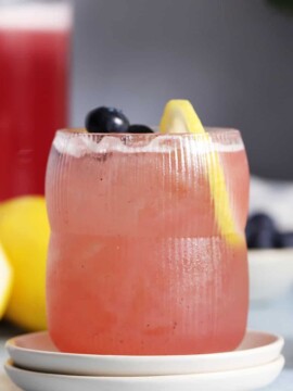 A glass of blueberry lavender lemonade garnished with fresh blueberries and a lemon slice.