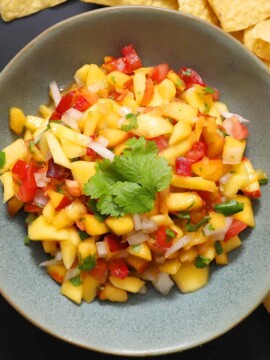 A blue bowl filled with mango peach salsa, garnished with cilantro leaves.