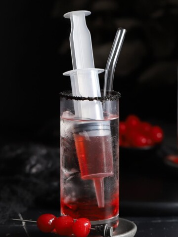 Glasses filled with lemon lime soda, ice, and syringes of grenadine syrup.
