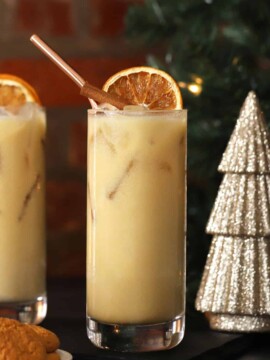 Two tall glasses of gingerbread mocktails garnished with dried oranges, cinnamon sticks, and straws.