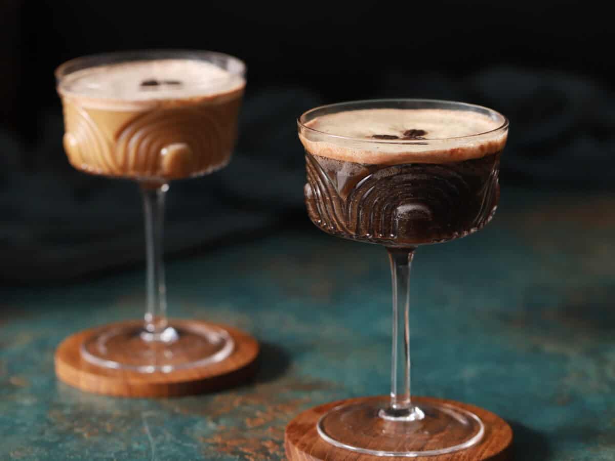 A pair of espresso martini mocktails on wooden coasters.