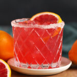 A glass of blood orange margarita garnished with a slice of blood orange.