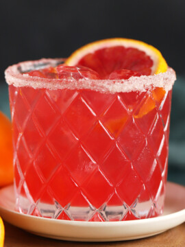 A glass of blood orange margarita garnished with a slice of blood orange.