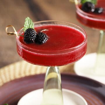 A martini glass filled with blackberry vanilla mocktail and garnished with fresh blackberries and mint.
