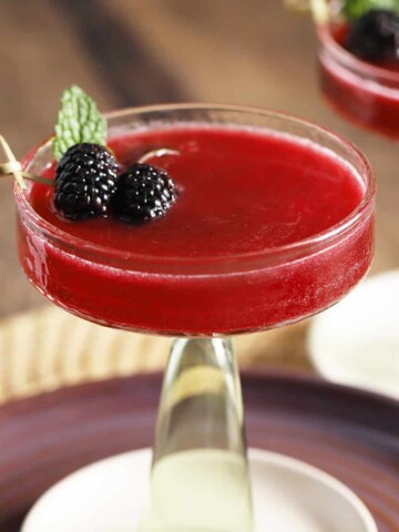 A martini glass filled with blackberry vanilla mocktail and garnished with fresh blackberries and mint.