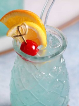 Looking down at a blue lagoon cocktail garnished with a slice of orange, lemon, and cherry.