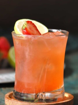 A glass of strawberry limeade mocktails garnished with fresh strawberries and slices of limes.