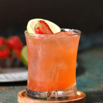 A glass of strawberry limeade mocktails garnished with fresh strawberries and slices of limes.