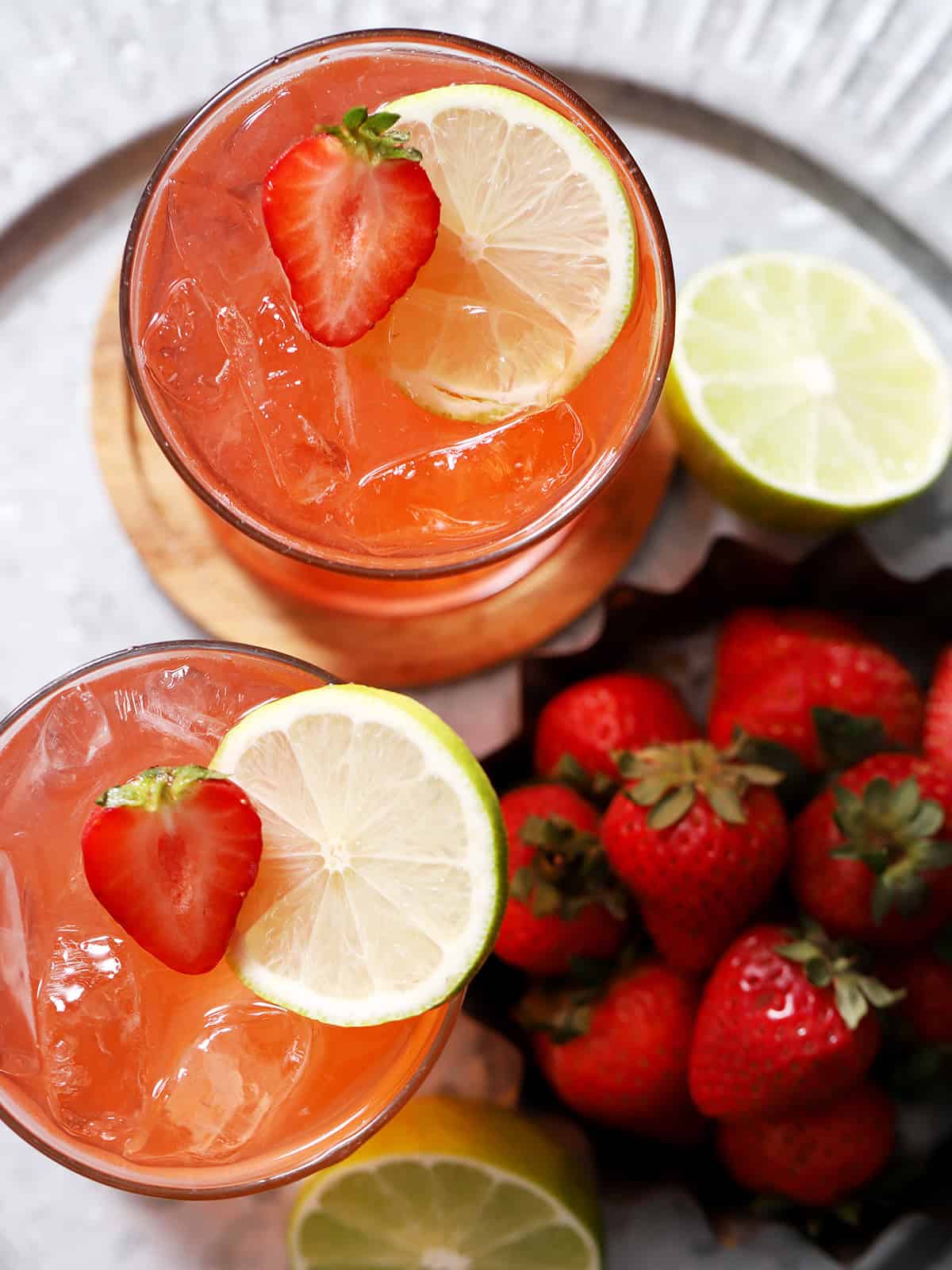 Looking down on two glasses of strawberry limeade mocktails garnished with fresh strawberries and slices of limes.