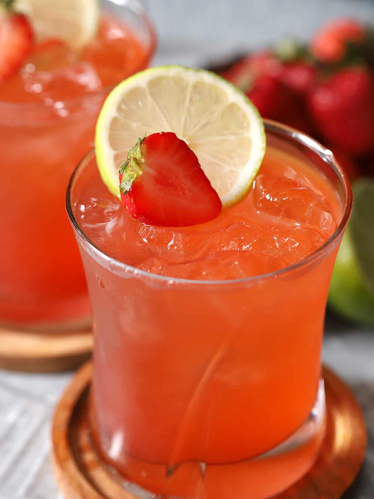 Two glasses of strawberry limeade mocktails garnished with fresh strawberries and slices of limes.
