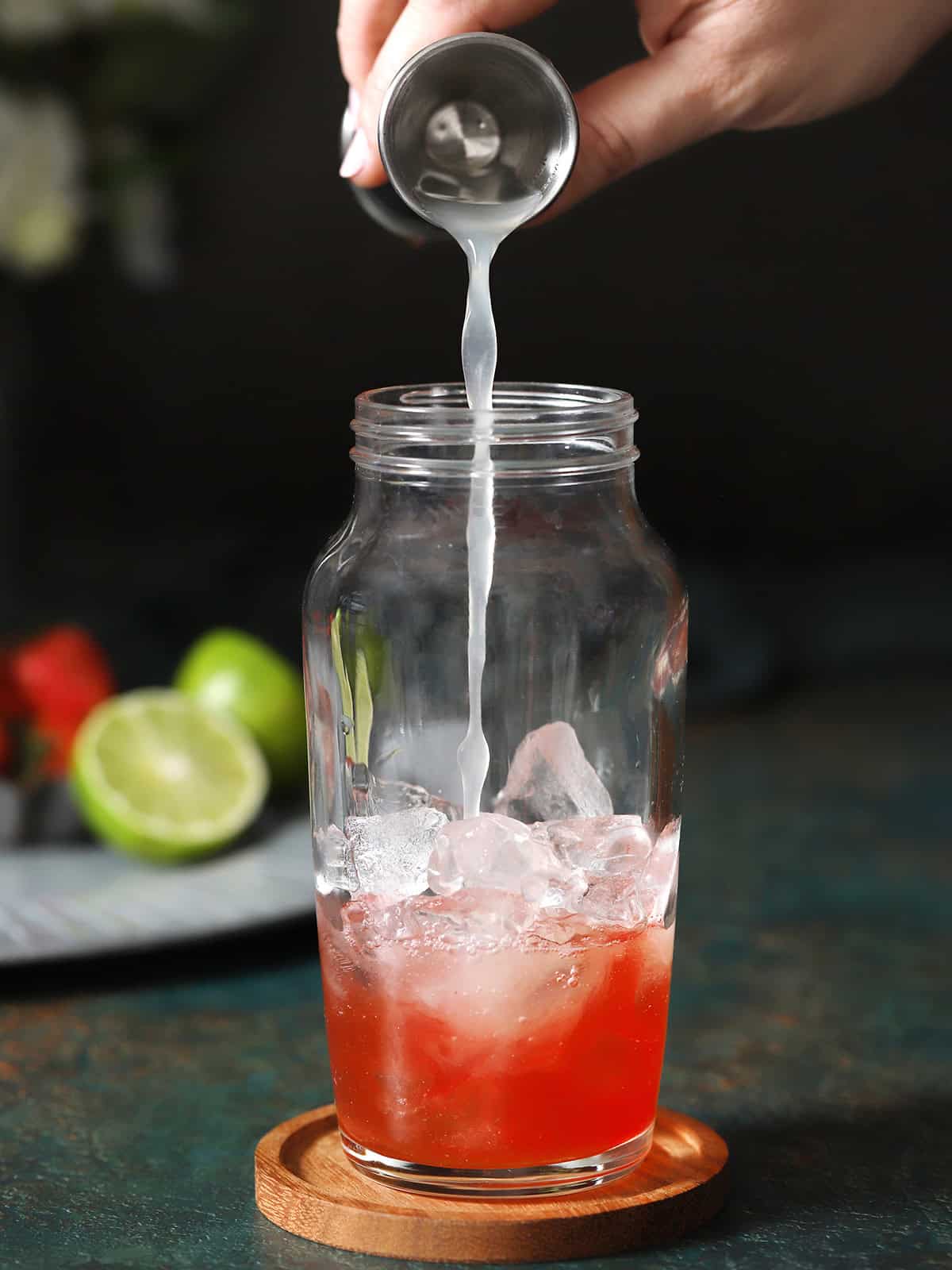 Lime juice being poured into a cocktail shaker with ice cubes in it. 
