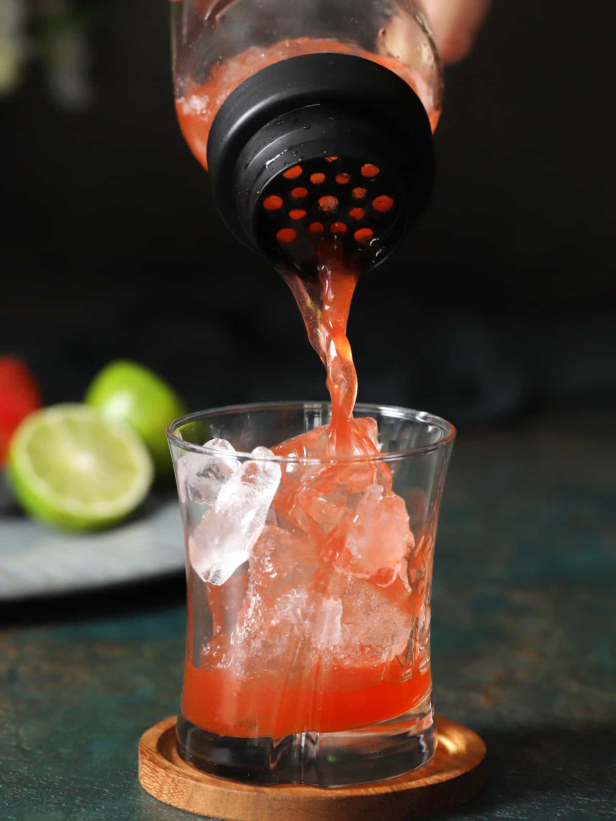 Strawberry Limeade mocktail being poured from a cocktail shaker into a rocks glass with ice. 