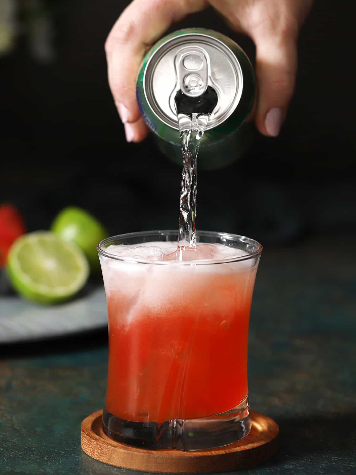 A hand pouring sparkling water into a glass of strawberry lime mocktail. 