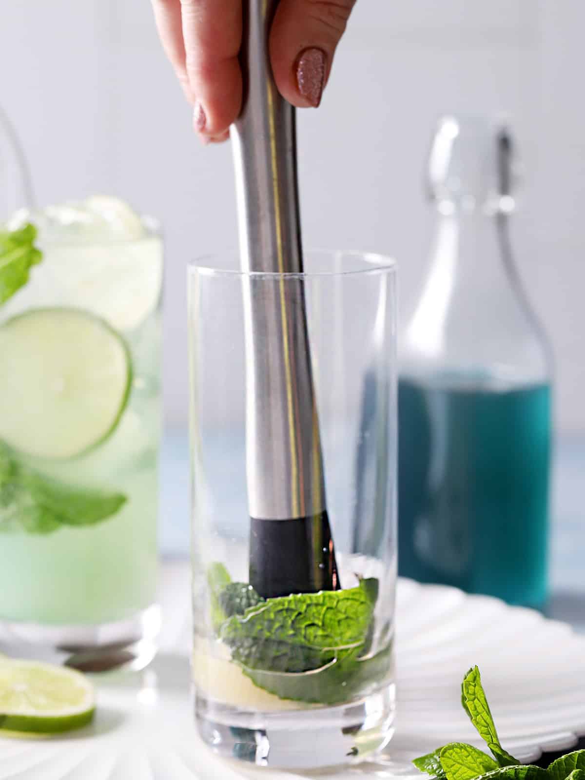 A hand placing a muddler in a tall glass. 