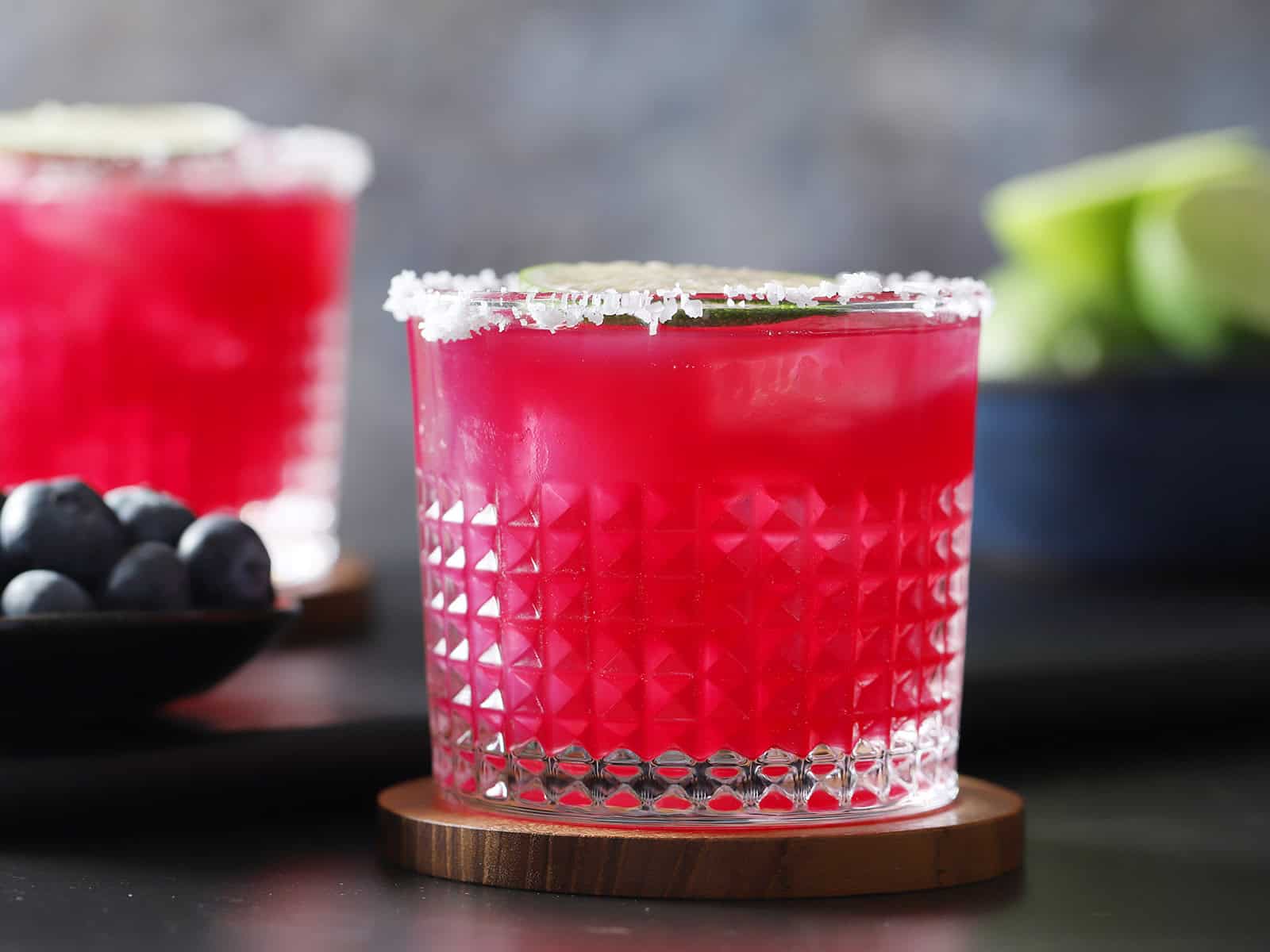 A glass with a salted rim filled with blueberry margarita.