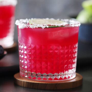 A glass with a salted rim filled with blueberry margarita.