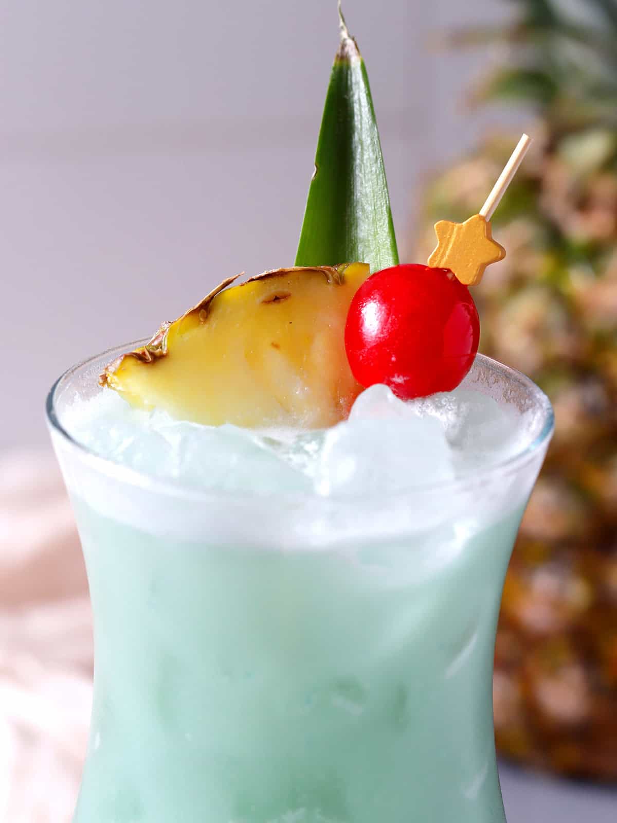 The pineapple leaf, pineapple slice, and cherry garnish on a blue hawaiian. 