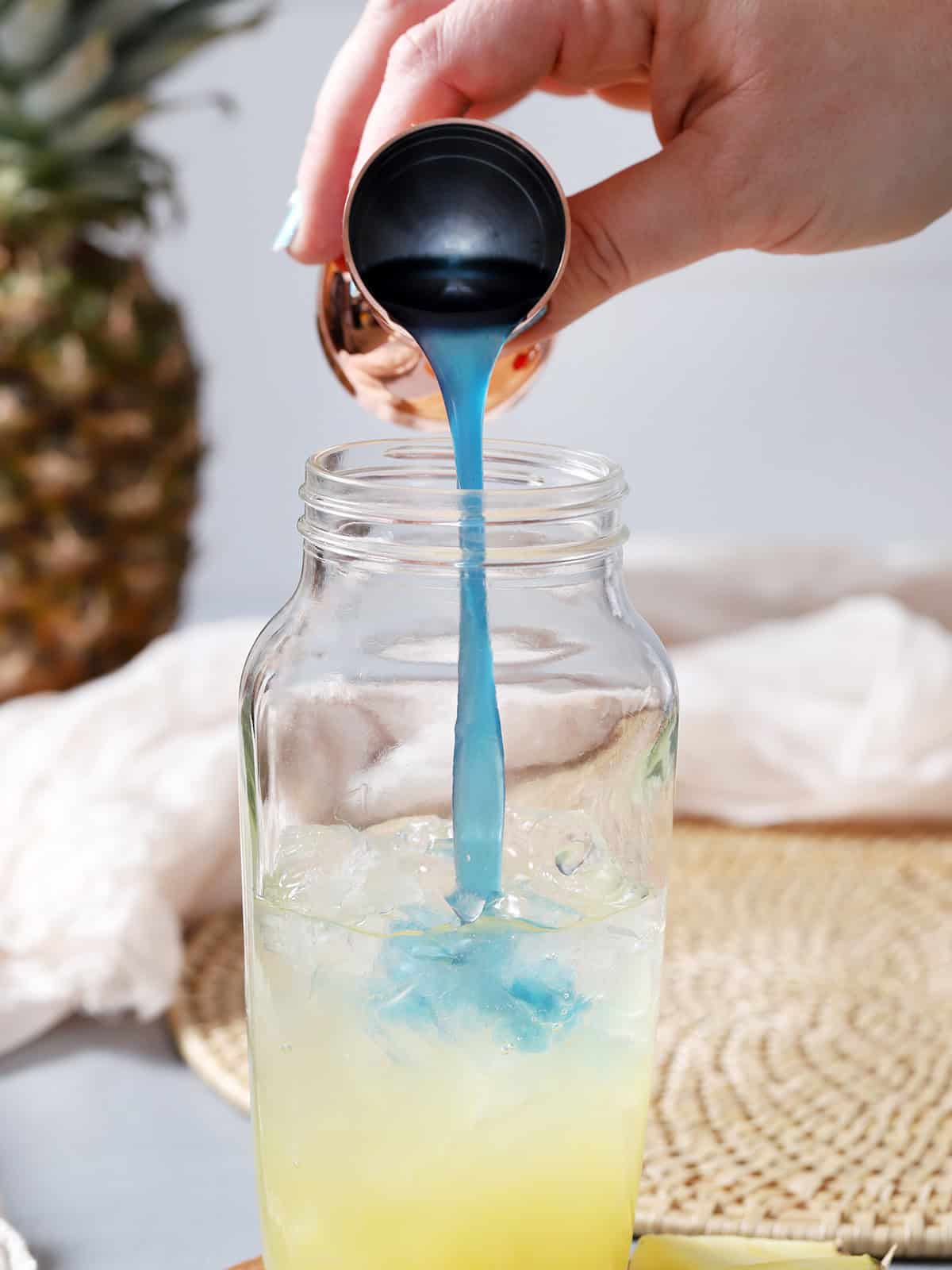 A hand pouring blue curaçao syrup into a cocktail shaker. 