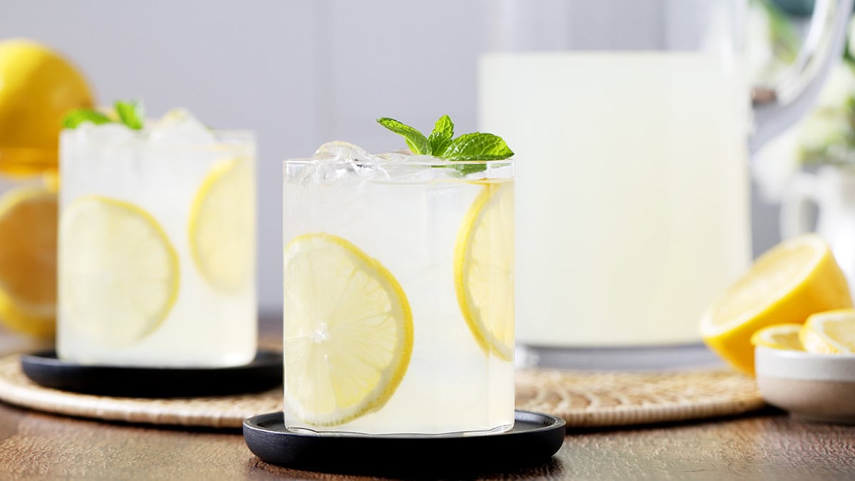 Two glasses and a pitcher filled with homemade lemonade, garnished with slices of lemons.